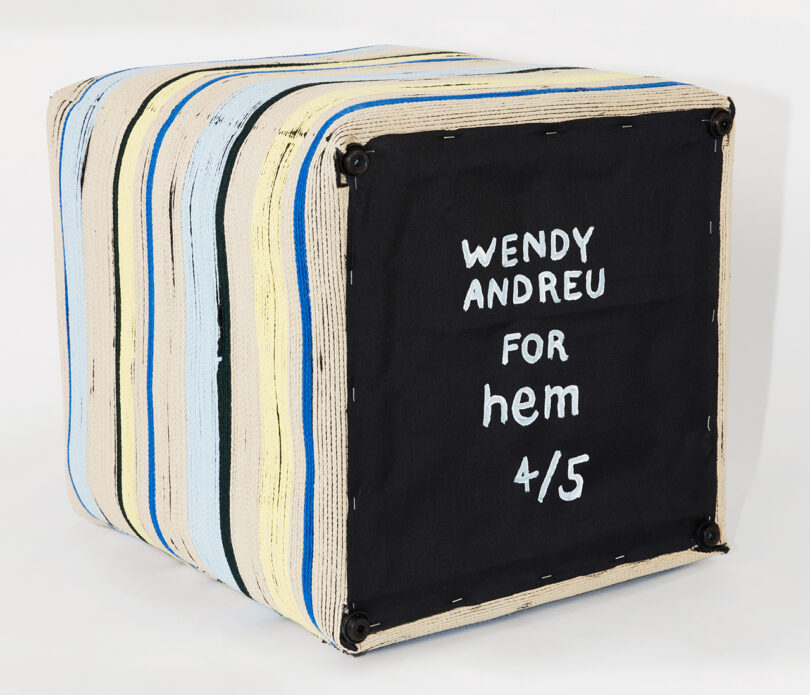bottom of detail of square stool with blue, black, yellow, and tan stripes reading Wendy Andreu for hem