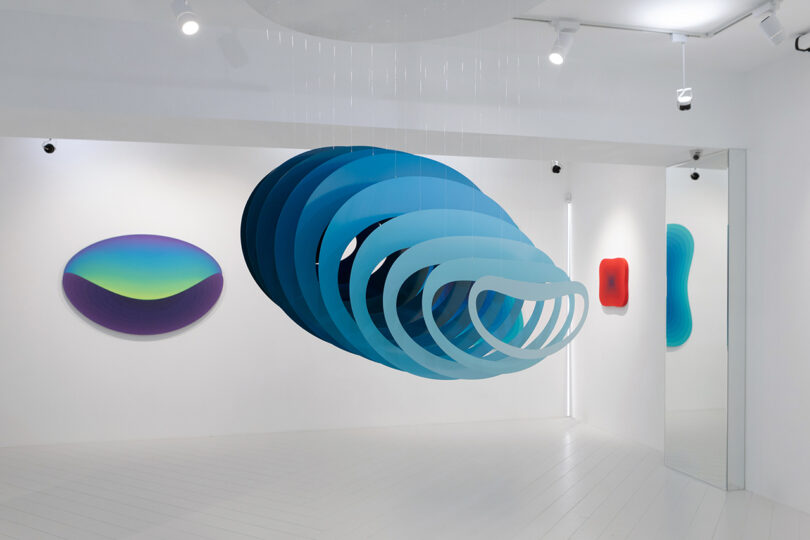 suspended blue spacial sculpture and oval-shaped blue art hanging on a white wall behind it