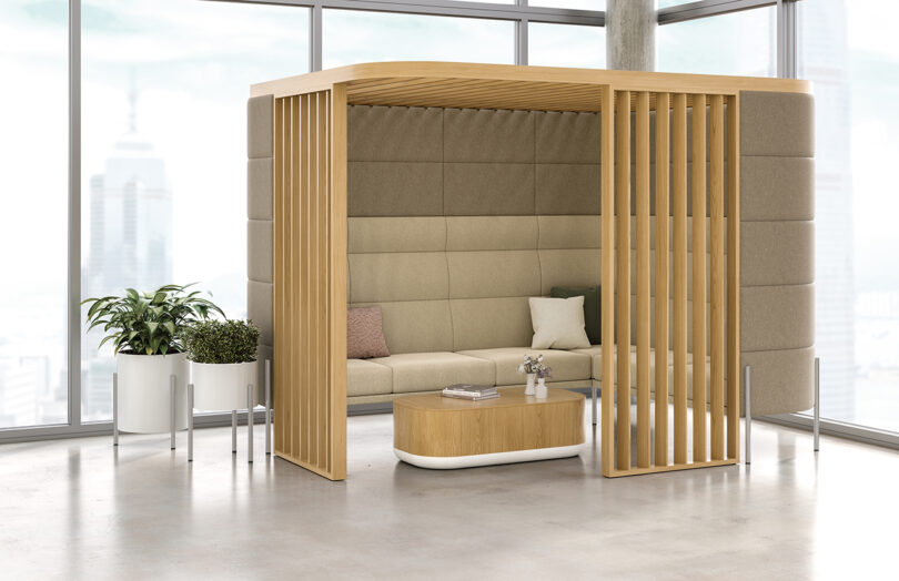 a privacy pod made of light wood slats and upholstered high back seating with a coffee table in a styled space