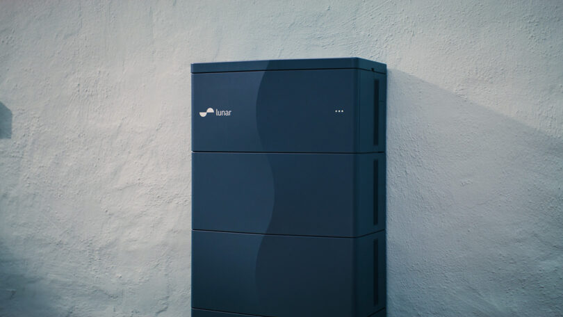 Lunar Energy battery system in dark blue set against a white exterior wall of a home.