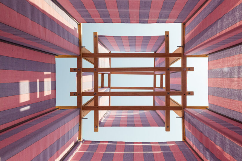 Interior upward view within the striped pink and blue temporary shade structure installed on the beach at Casa Naila. 