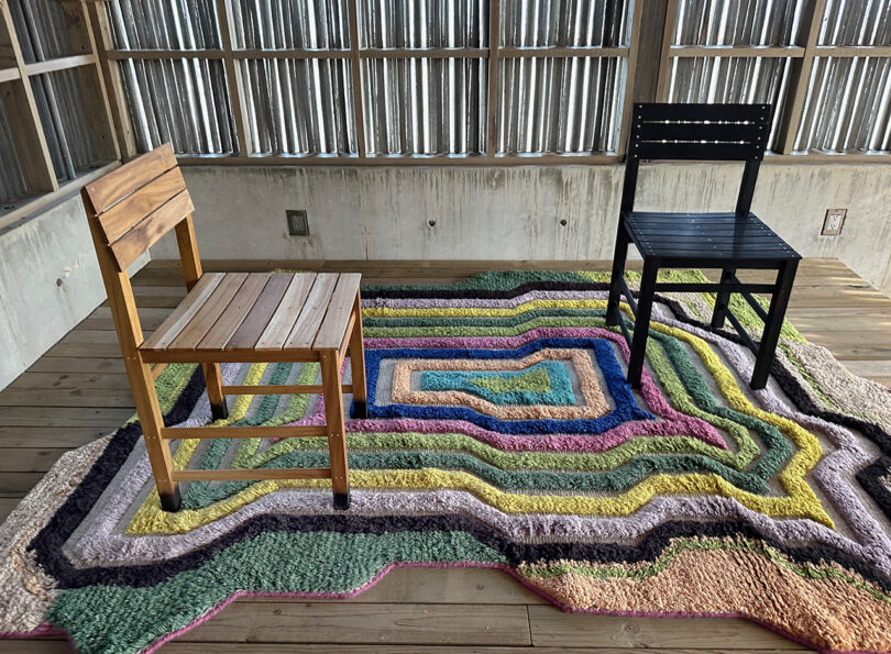 Multicolor chromatic geometric design wool rug with a pair of wood chairs set across it.
