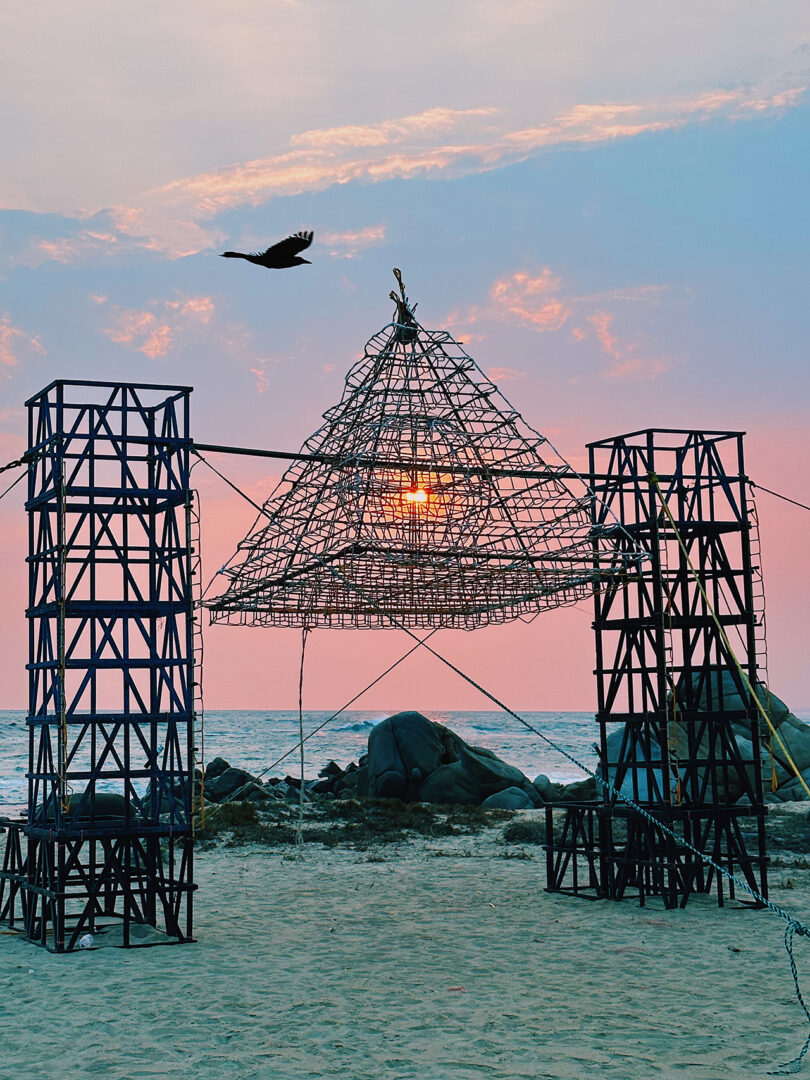 Pyramid shaped Mexican portablepyrotechnic frame structure with coastal sunset in the background and seabird silhouette flying in the foreground.