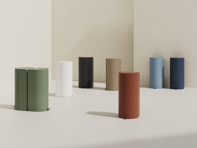 seven tall cylindrical garbage cans in various muted tones