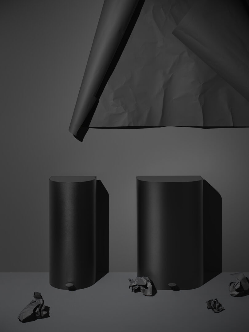 two tall black cylindrical garbage cans against a black wall