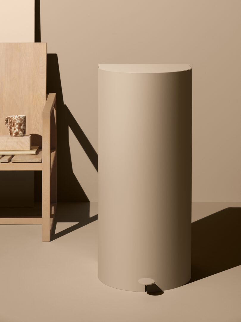 tall beige cylindrical garbage can against a beige wall