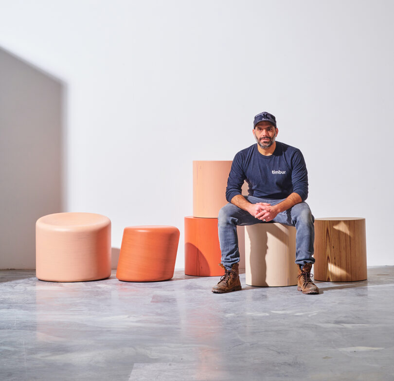 light-skinned man sitting on a short stool and surrounded by others in warm pastels tones