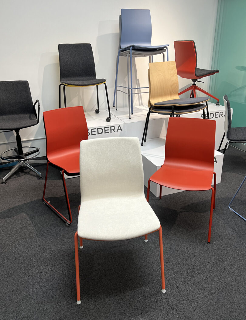 eight dining and office chairs of differing styles and colors on a podium