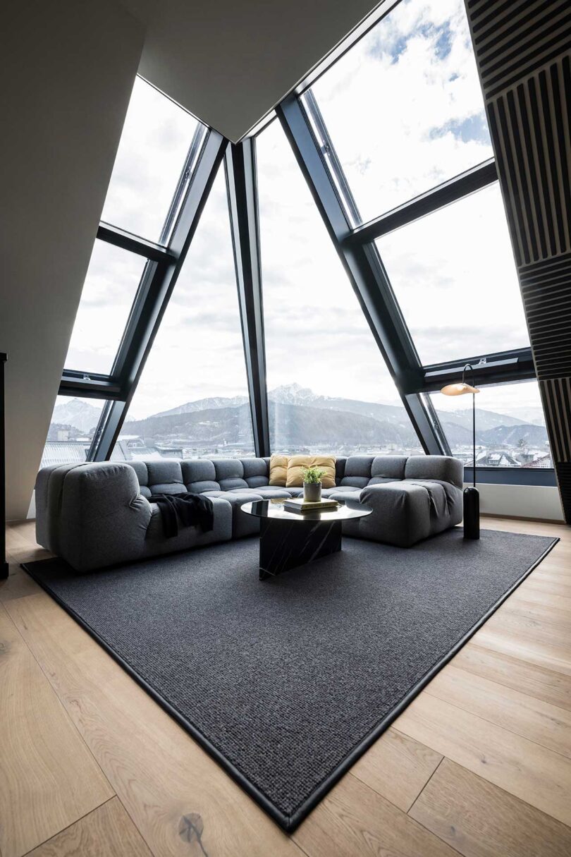 interior de apartamento moderno com paredes de vidro inclinadas e sofá cinza secional