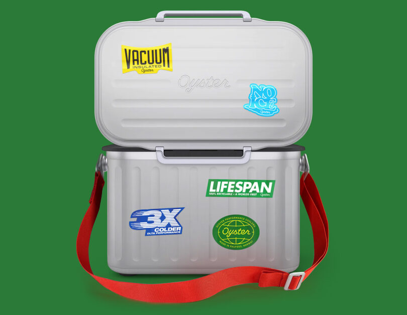 Oyster Tempo Performance Cooler covered in stickers with red shoulder strap with top lid open with green backdrop.