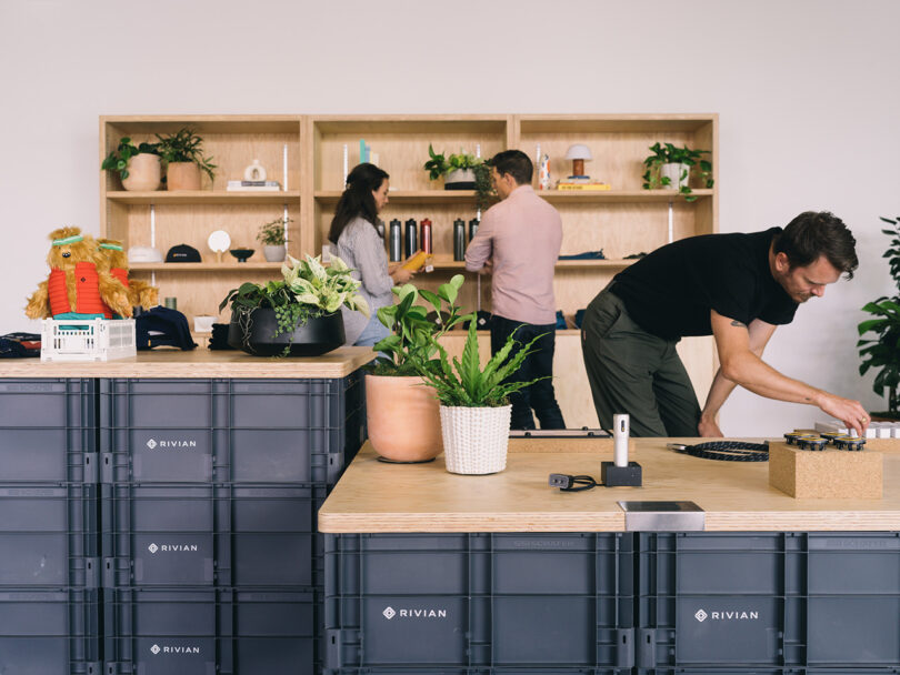 Interior of Rivian Spaces High Line, with wood shelves displaying Rivian branded accessories with three people browsing.