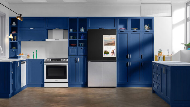 New Samsung Bespoke refrigerator with 32-inch screen on left upper door staged in a contemporary kitchen setting with blue cabinetry.