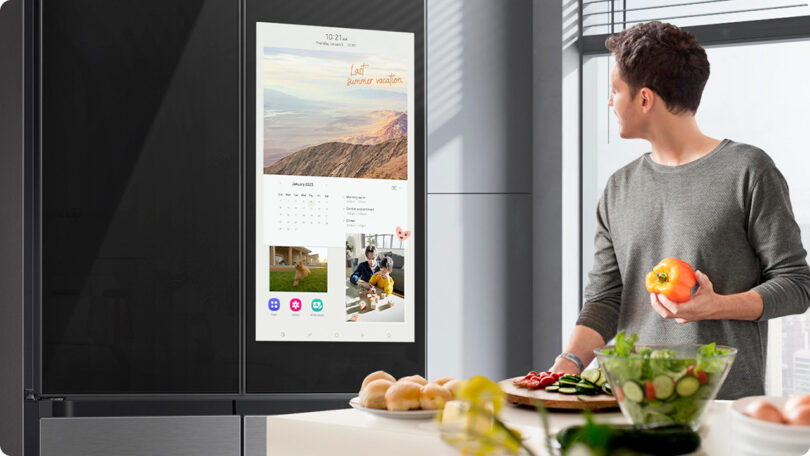 Man in gray sweater looking at 32" Family Hub display integrated into refrigerator door.