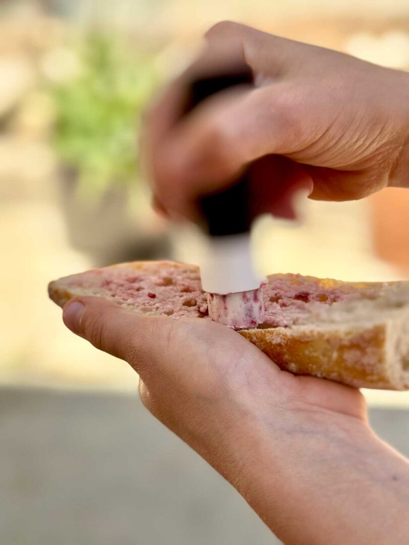 raspberry and butter being spread onto cut baguette