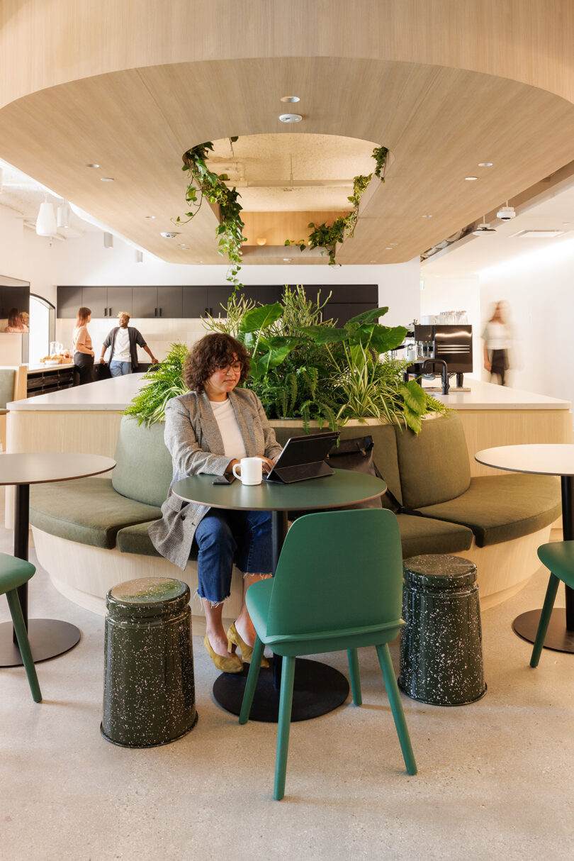 Woman at green round table seated at her laptop at Tinder's in-house coffee cafe seated around a circular built-in cushioned seating area.