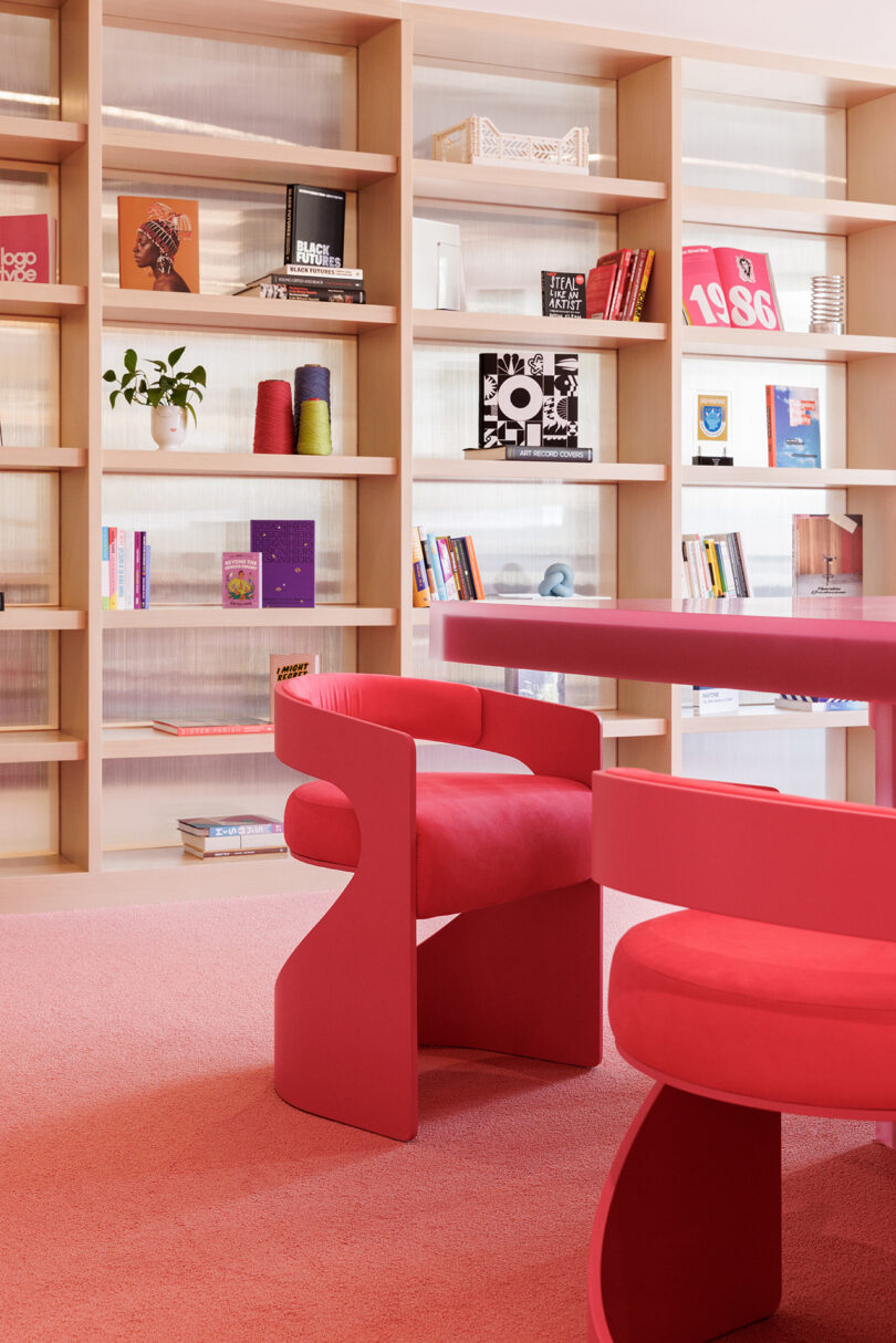 A custom hot-pink central table with cutouts and bookshelves filled with a few books and design objects, with muted pink carpeting.