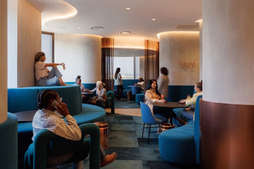 Nine Tinder employees standing and seated across various plush deep blue upholstered seats undulating across a muted blue checker carpeted floor.