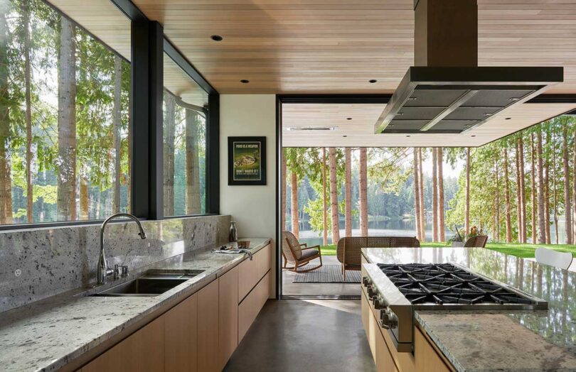 view through modern kitchen with light wood cabinets to outdoor deck through opened sliding glass doors