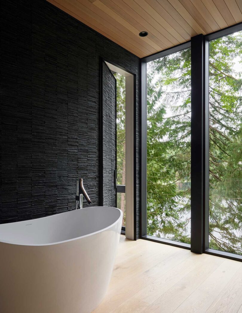 نمای زاویه‌دار حمام مدرن با دیوار سیاه، پنجره‌ها و وان سفید
