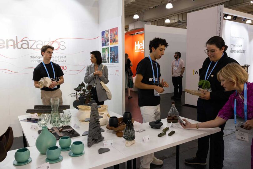angled view of booth at trade show with design objects on tables with people standing aroudn