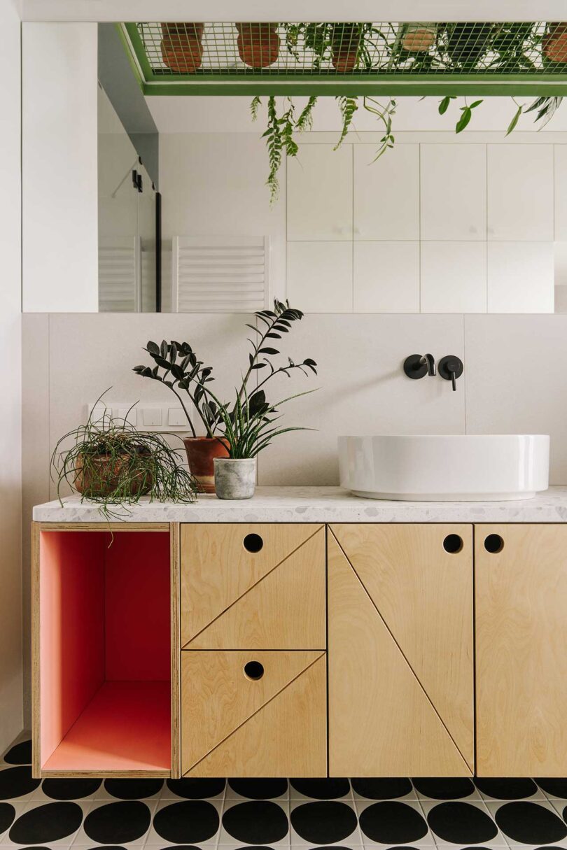 Częściowy widok nowoczesnej łazienki z różowym schowkiem i geometryczną drewnianą szafką z czarno-białymi płytkami podłogowymi
