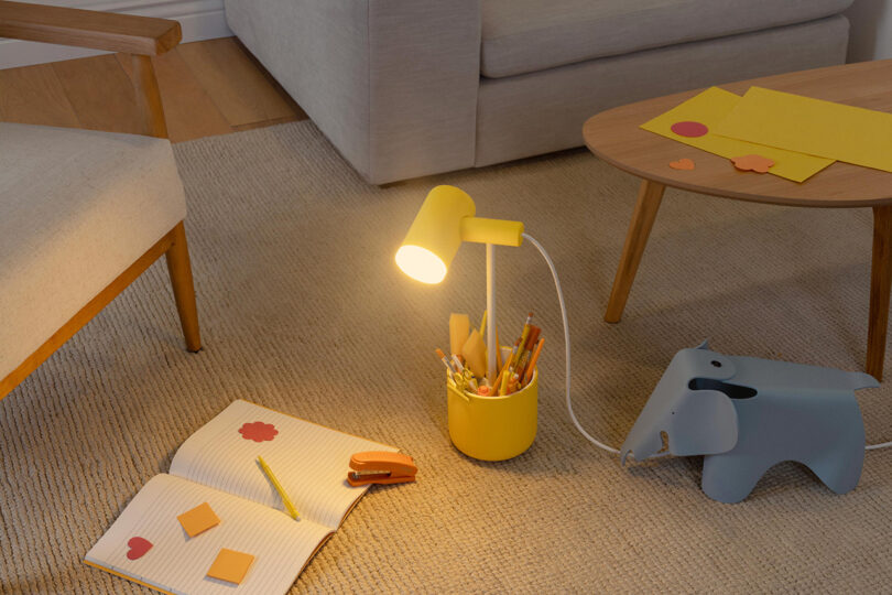 Yellow portable task light with caddy base on rug floor illuminating a notebook. 