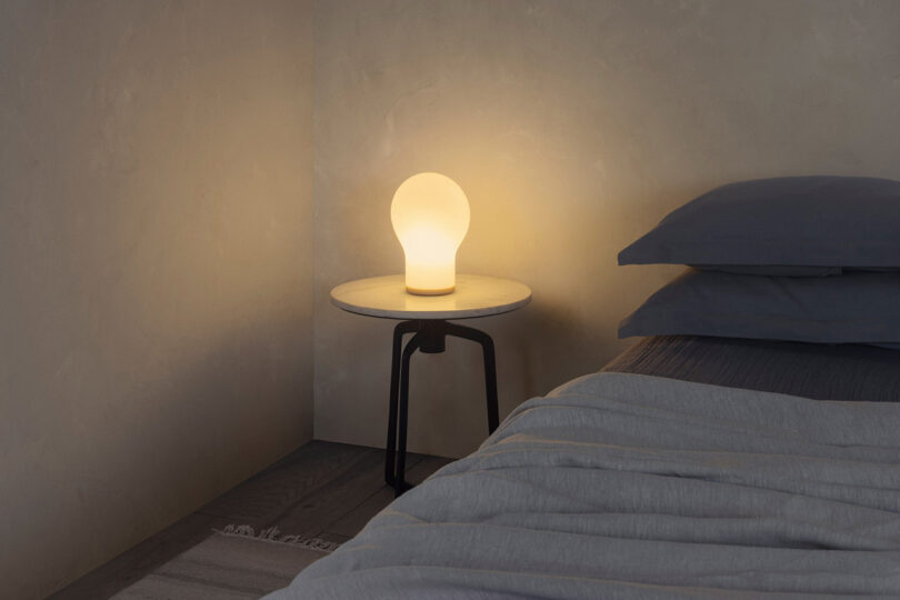 Large light bulb shaped table lamp set in bedroom corner glowing softly as mood light.
