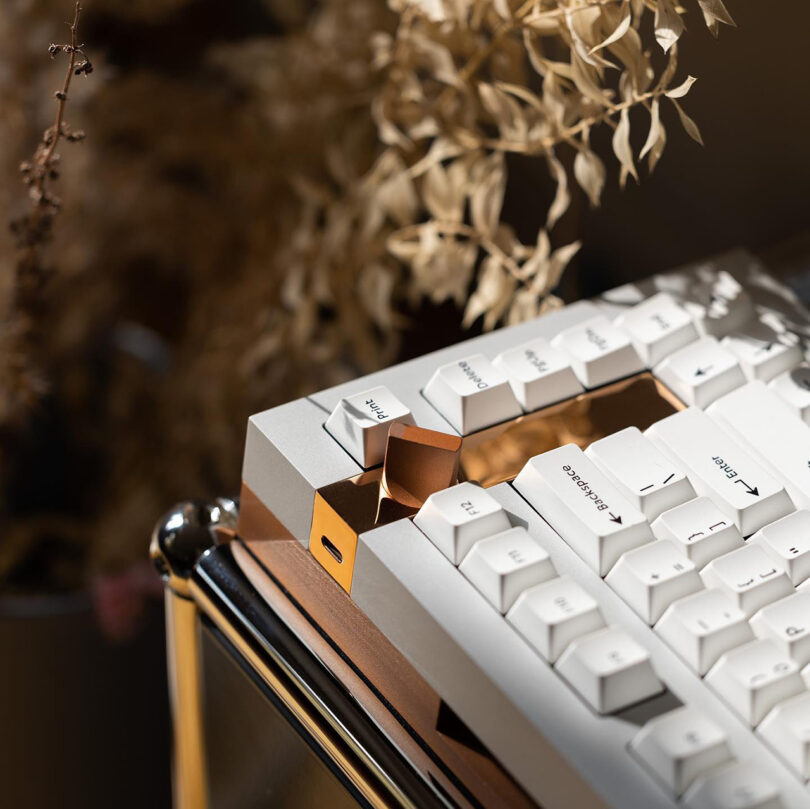 Close up corner view of geistmaschine mechanical keyboard in white and bronze showing the USB-C port, dial control, and bronze detailing.