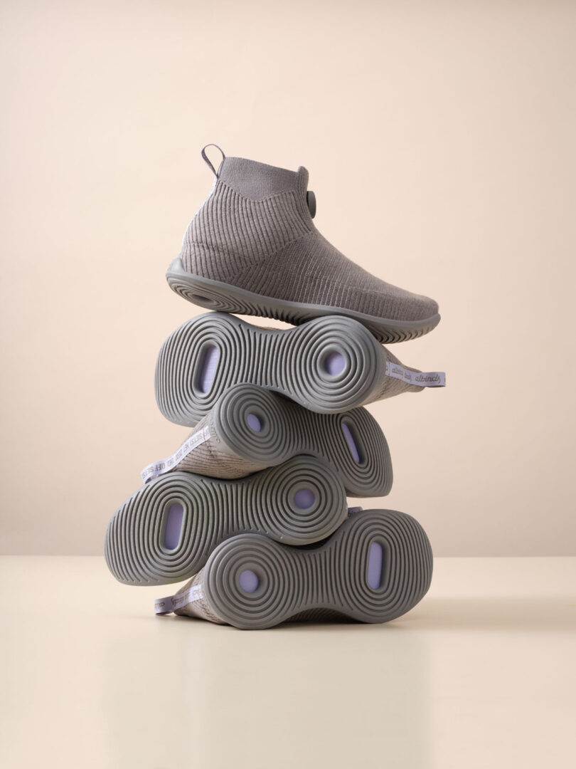 A pile of five Allbirds Moonshot sneakers stacked on top of one another against a beige surface and wall background.
