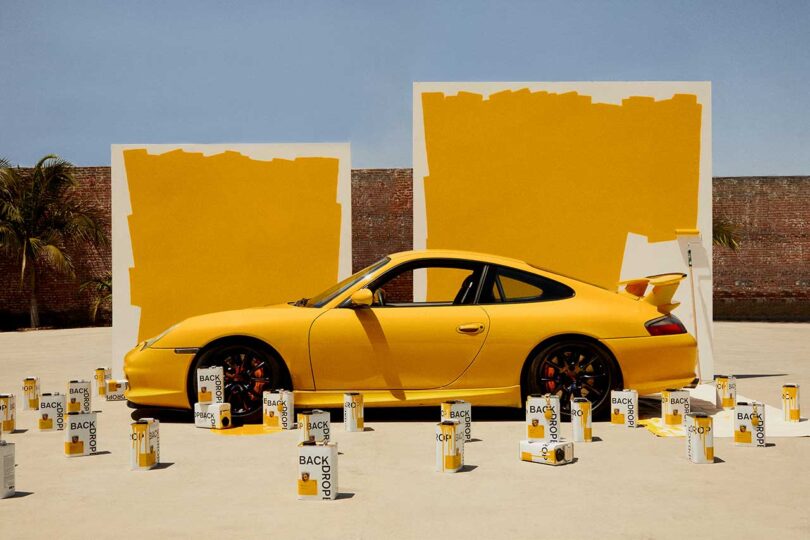 angled view of golden yellow colored vintage Porsche with matching large paint swatch in back and cans of golden yellow paint in front