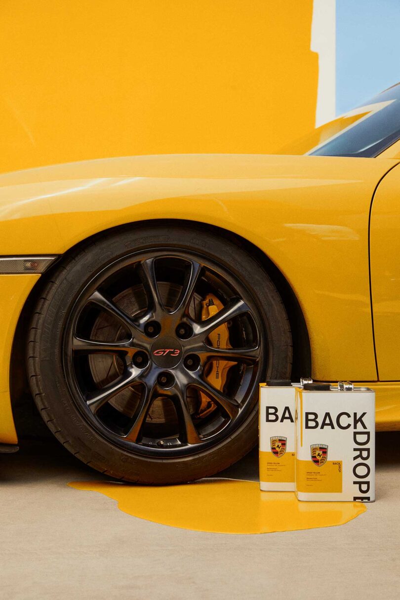 close up partial view of vintage porsche painted golden yellow with cans of spilled paint in front