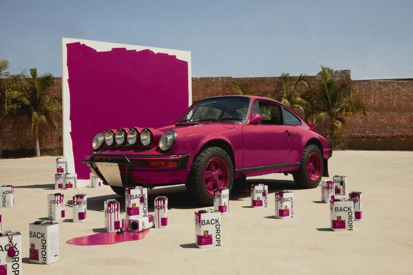 angled view of magenta colored vintage Porsche with matching large paint swatch in back and cans of magenta paint in front