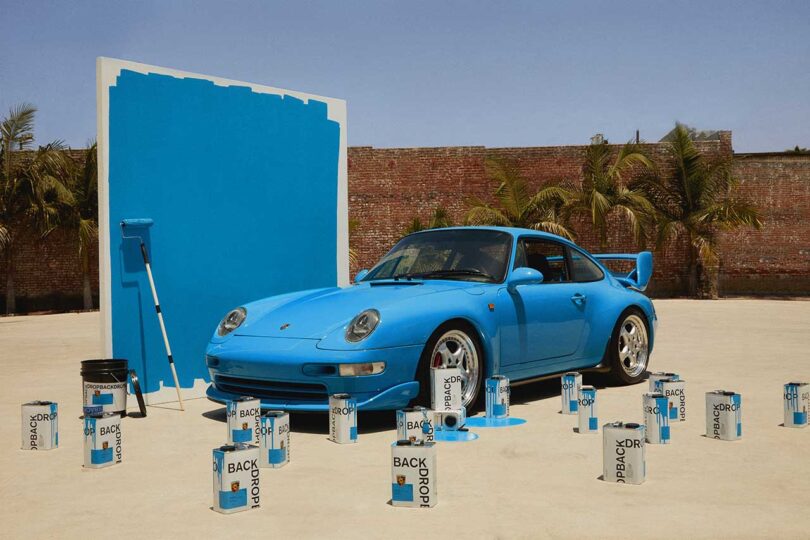 angled view of sky blue colored vintage Porsche with matching large paint swatch in back and cans of sky blue paint in front