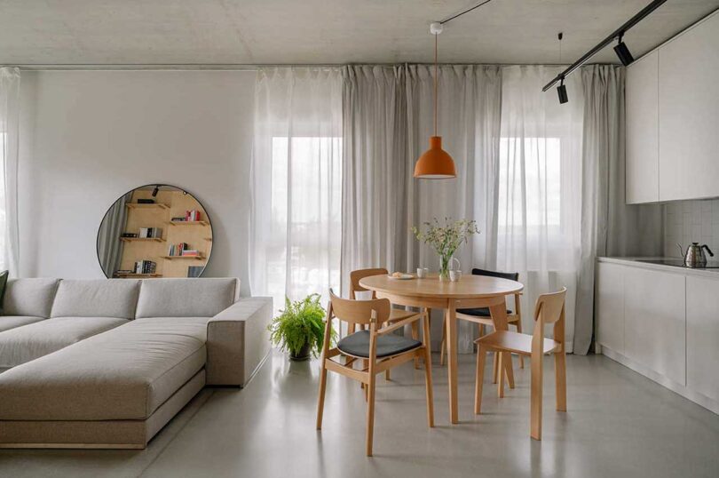 partial view of open layout in modern apartment showing part of modular grey sofa, round dining table and chairs, and white kitchen