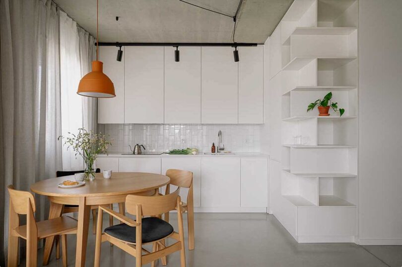 view into minimalist white kitchen in modern apartment with small wood dining set