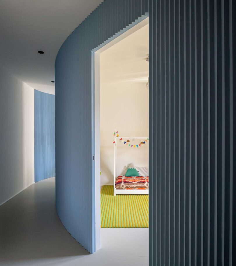 curved hallway view with blue fluted walls looking into kid's room
