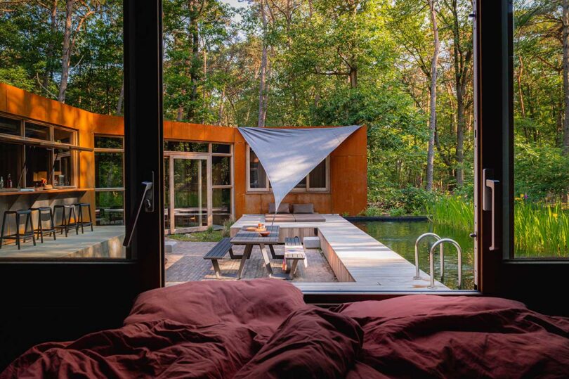 view from bed through opened window out to modern home's deck and pool