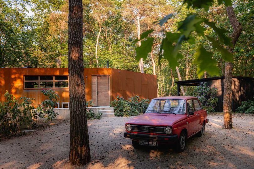 partial exterior view of modern house cabin clad in corten steel in woods with vintage red car
