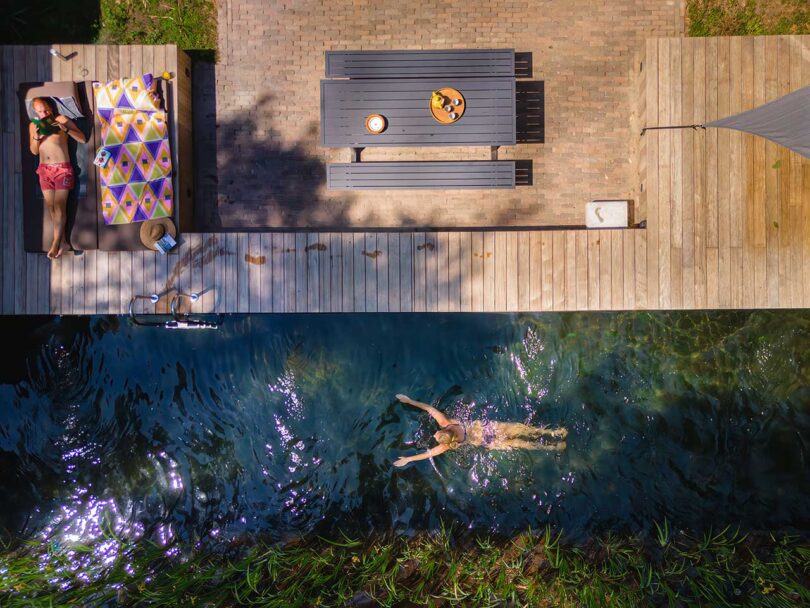 drone view looking down at modern house with deck and pool with someone swimming 