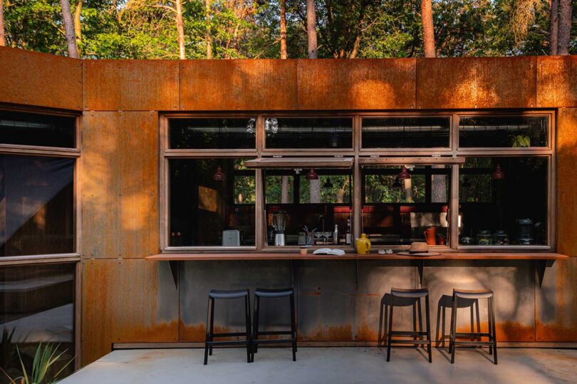 partial exterior view of modern home with corten steel exterior with bar that extends inside into the kitchen