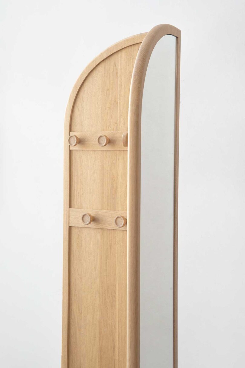 partial closeup view of light wood arch-shaped bi-fold floor mirror in styled space