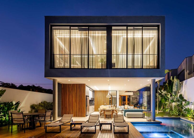 exterior view of modern home's rear at sundown with lights on and views of the pool