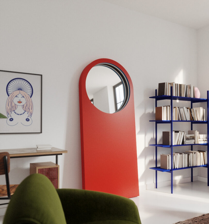 round mirror at the top of a large red floor mirror in a styled space