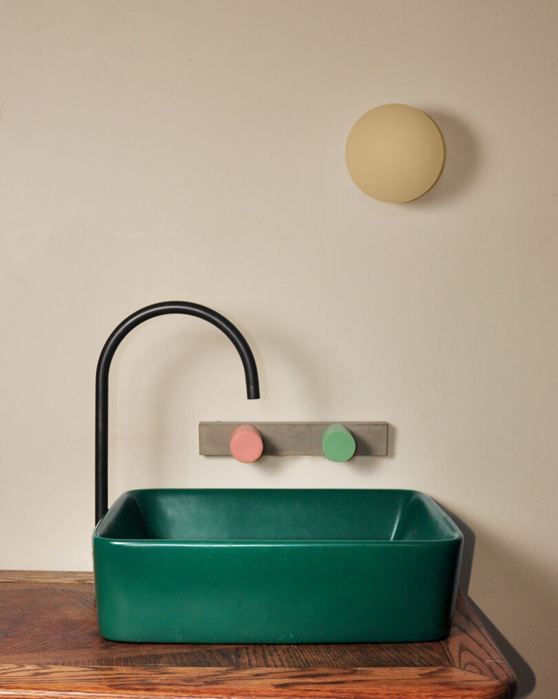 dark green bathroom sink with black faucet and light pink and light green faucet handles