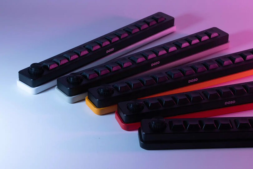 Five single row macro pad keyboards in various colors set against a gradient background bathed in blue and pink lighting