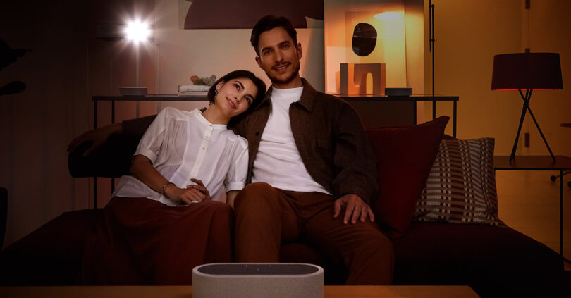 Young woman has her head resting upon shoulder of man while they watch a movie paired with Sony HT-AX7 home theater audio speaker system.