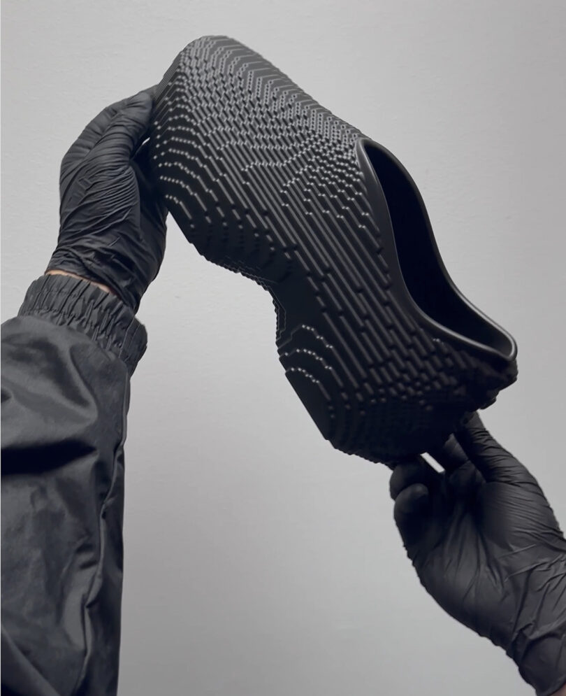 Black gloved hands holding up Pixel Rider foam sneakers at an angle with toebox up.