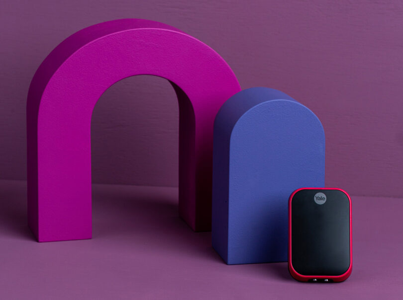 Yale Assure Lock 2 with a Viva Magenta color case finish, the Pantone’s Color of the Year 2023, set to the right alongside several colorful abstract shapes.