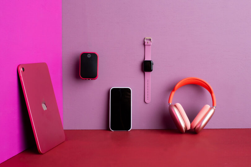Yale Assure Lock 2 with a Viva Magenta color case finish wall mounted alongside an Apple iPad, iPhone, Apple Watch and AirPods Max in hues of red, pink and magenta.
