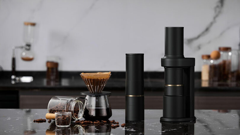 Cocinare Essence grinder in both portable and table top mode next to a pour-over setup with glass coffee mugs to the left in a kitchen setting.